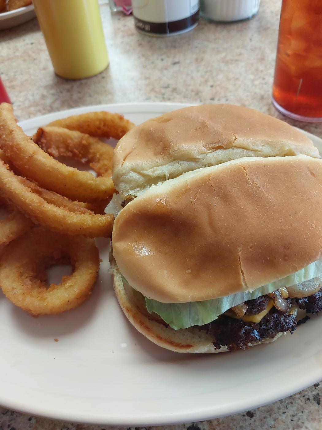 Two cheeseburgers with grilled onions and lettuce beside a stack of onion rings