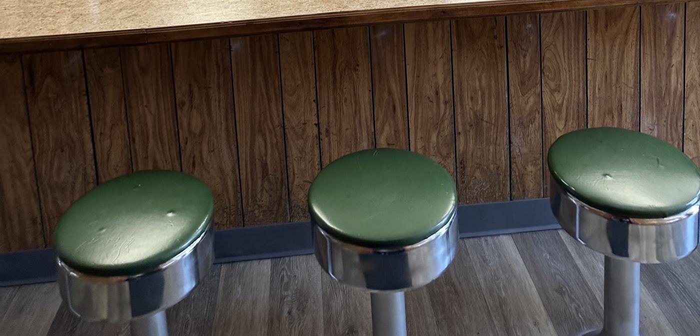 Three green swivel stools on polished pedestals along the panelled front of the counter